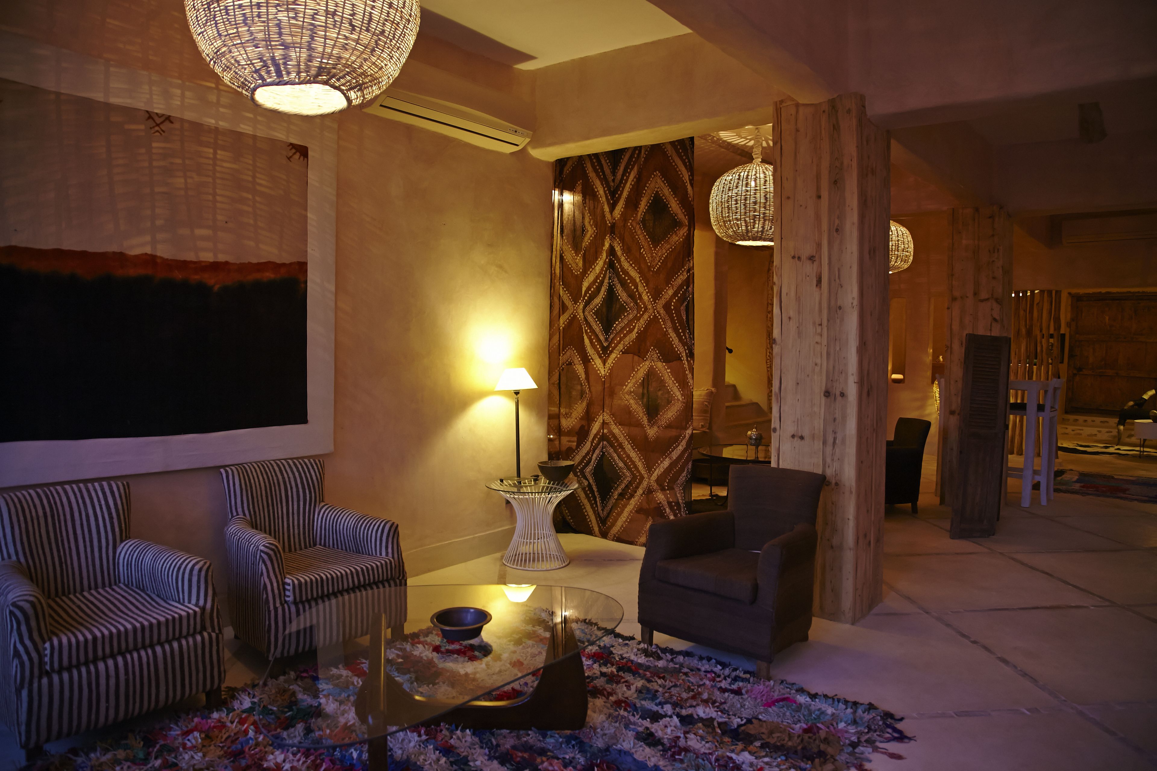 Un salon moderne avec des fauteuils à rayures, une table basse en verre et un mur orné d’un motif.