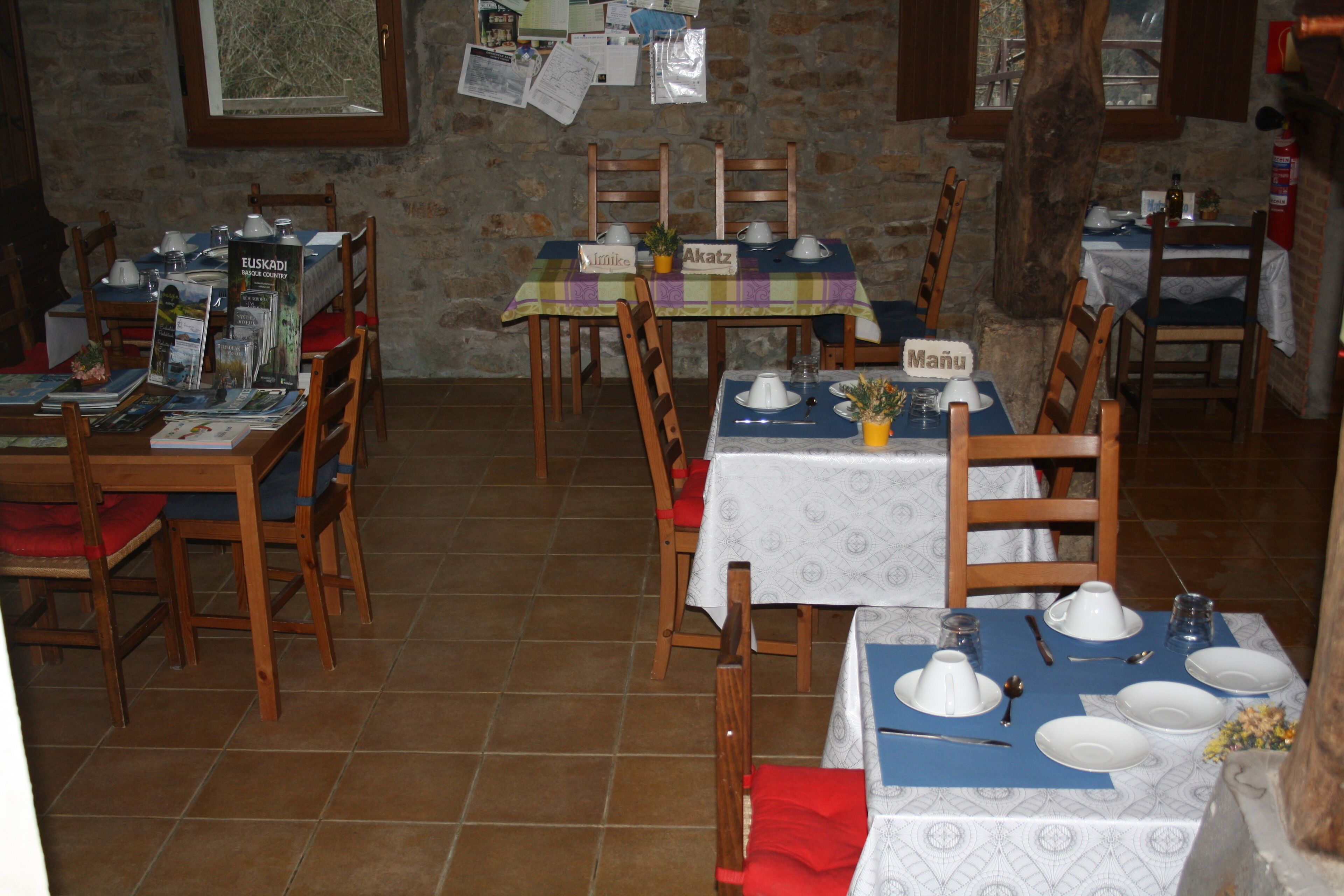 A restaurant with multiple tables set for dining, wooden chairs, and a stone wall background.