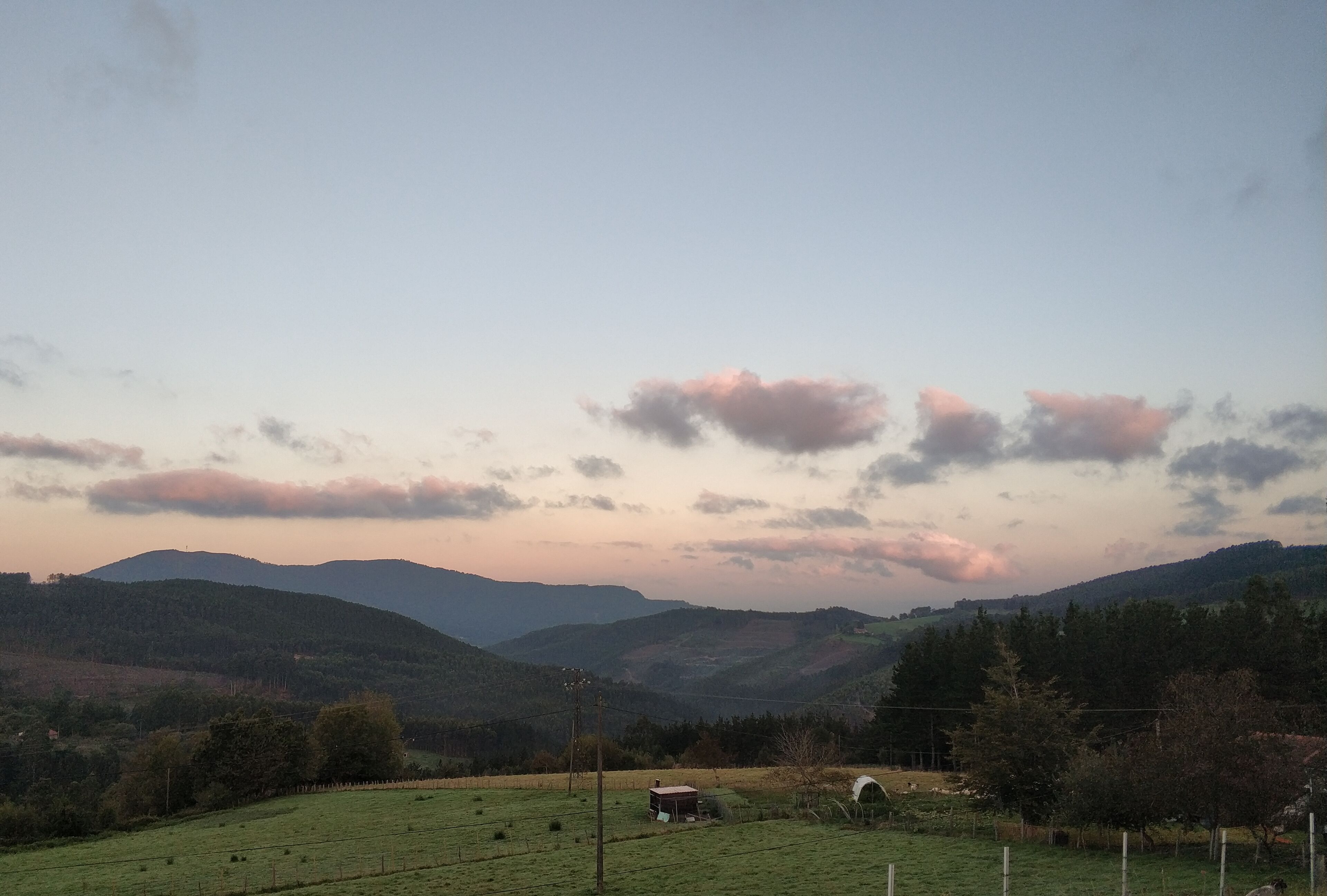 Un paysage rural avec des collines douces, un champ clôturé et un petit bâtiment au premier plan.
