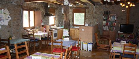 A rustic dining area with wooden tables and chairs, stone walls, and a clock.