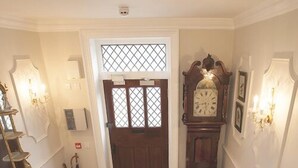A staircase leading to a door with a patterned floor, a wall-mounted clock, and a radiator. - Victoria House Stow (Cheltenham)