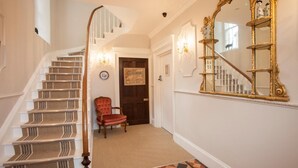 A grand staircase with a wooden handrail, a red chair, and a large ornate mirror on the wall. - Victoria House Stow (Cheltenham)
