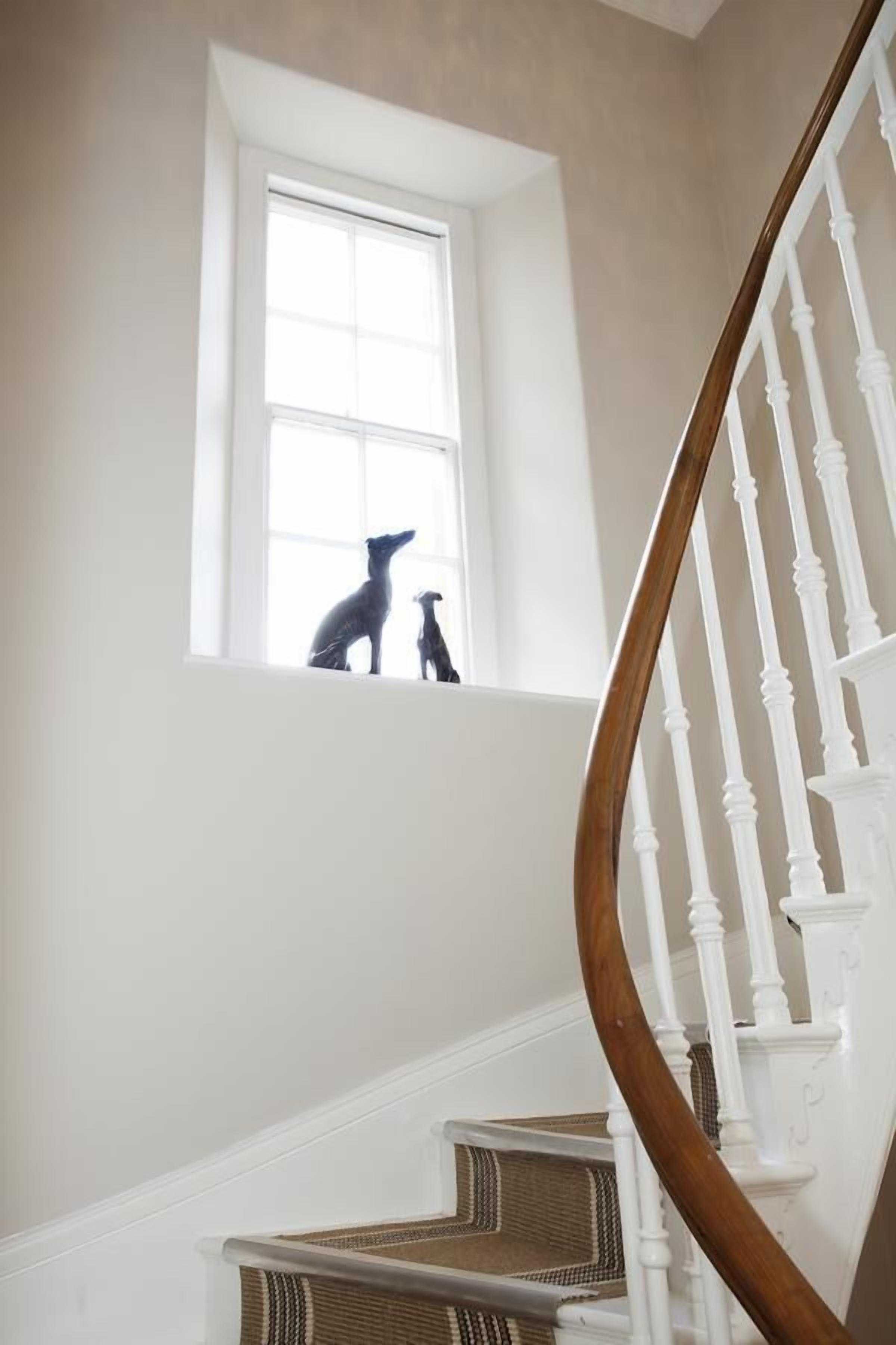 A staircase with white balusters and a wooden handrail, leading to a landing with a window.