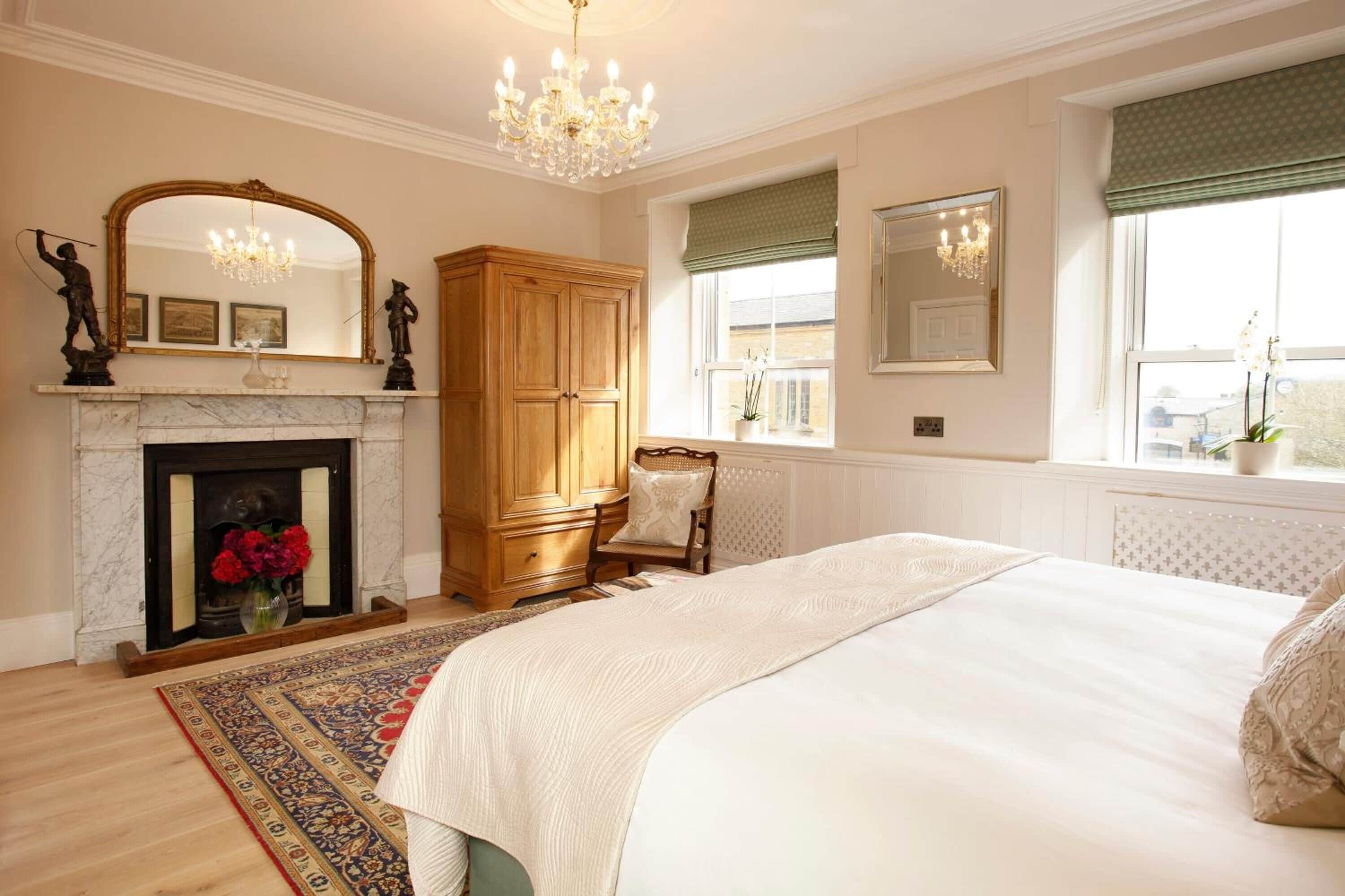 A bedroom with a large bed, a fireplace, a wooden wardrobe, and a window with a view.