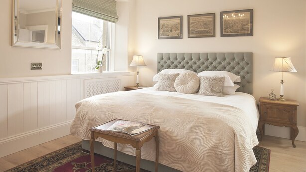 A bedroom with a large bed, two bedside tables, a window with curtains, and three framed pictures on the wall. - Victoria House Stow (Cheltenham)