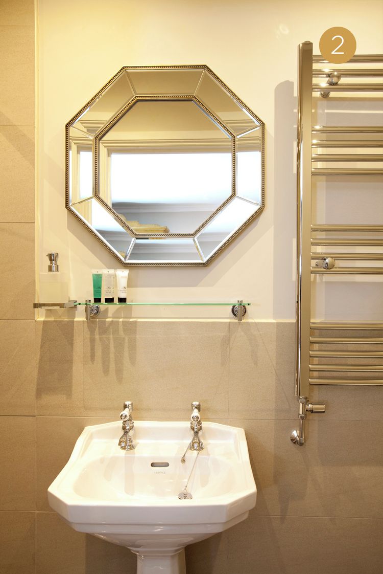 Un baño con lavamanos blanco, un espejo hexagonal y un perchero para toallas.