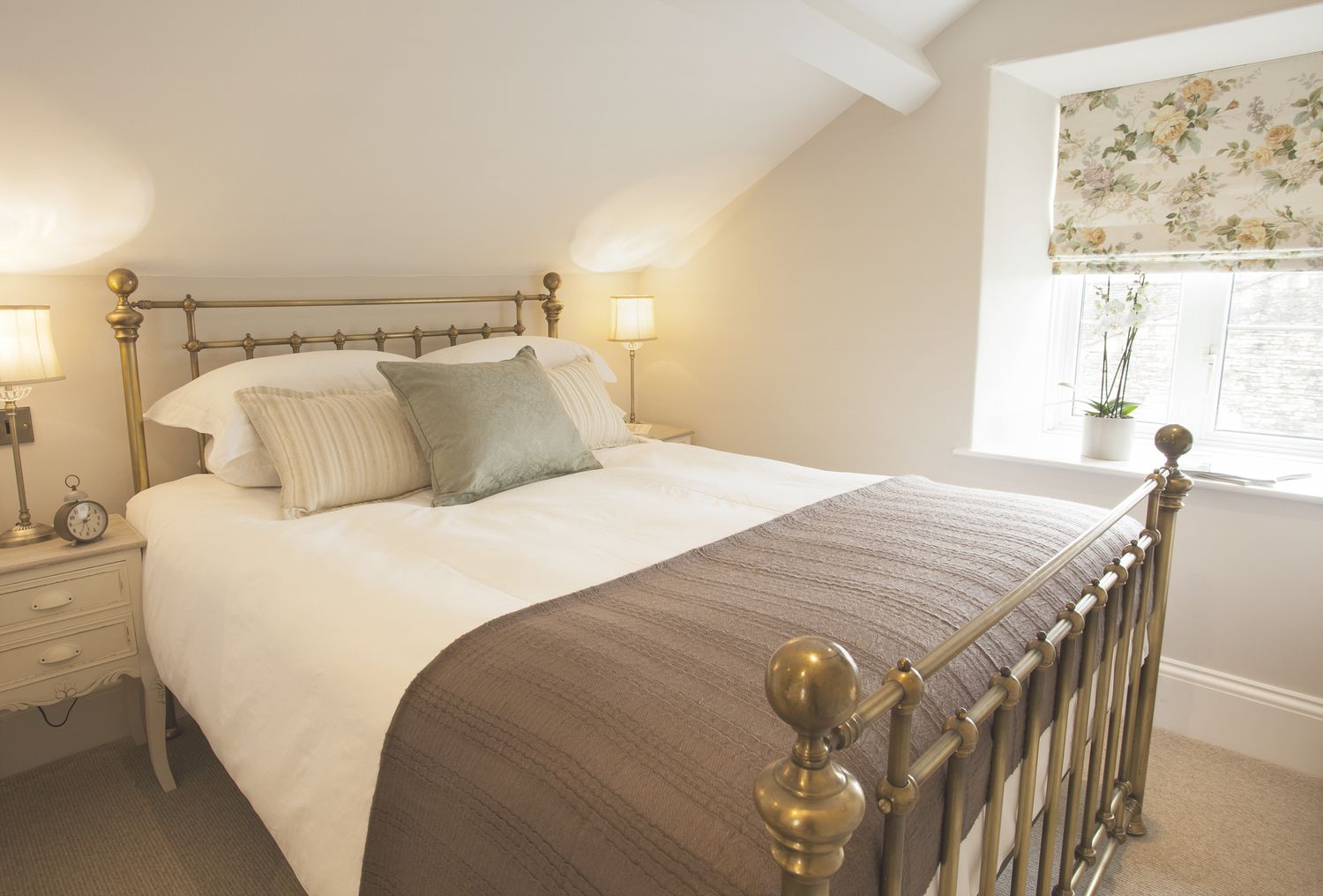A neatly made bed with a wooden headboard, a bedside table with a lamp, and a window with a floral curtain.