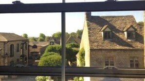 A window view of a stone building with a traditional roof, a small attached structure, and a clear sky. - Victoria House Stow (Cheltenham)