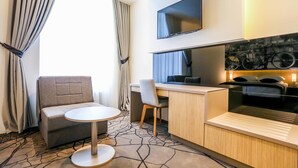 Une chambre d’hôtel comprenant un canapé, une petite table ronde, un bureau avec une chaise, un téléviseur à écran plat fixé au mur et un coin cuisine équipé d’un four à micro-ondes et d’une cuisinière.