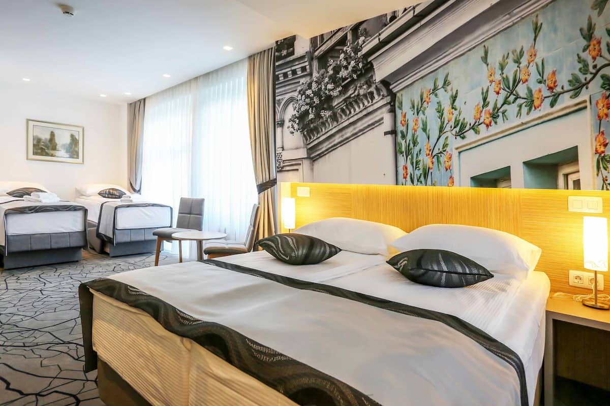 A hotel room with a large bed, two smaller beds, a chair, a table, and a mural on the wall.
