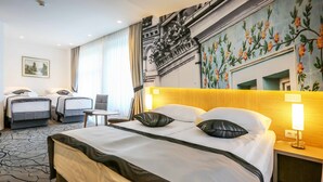 Une chambre d’hôtel avec un grand lit, deux petits lits, une chaise, une table et une fresque murale.