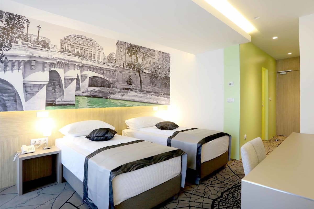 A hotel room with two beds, a desk, and a wall mural.