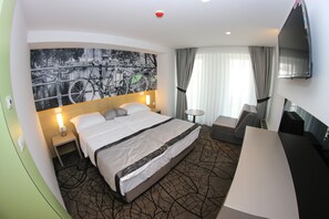 A hotel room with a large bed, a desk, a TV, and a wall-mounted TV.