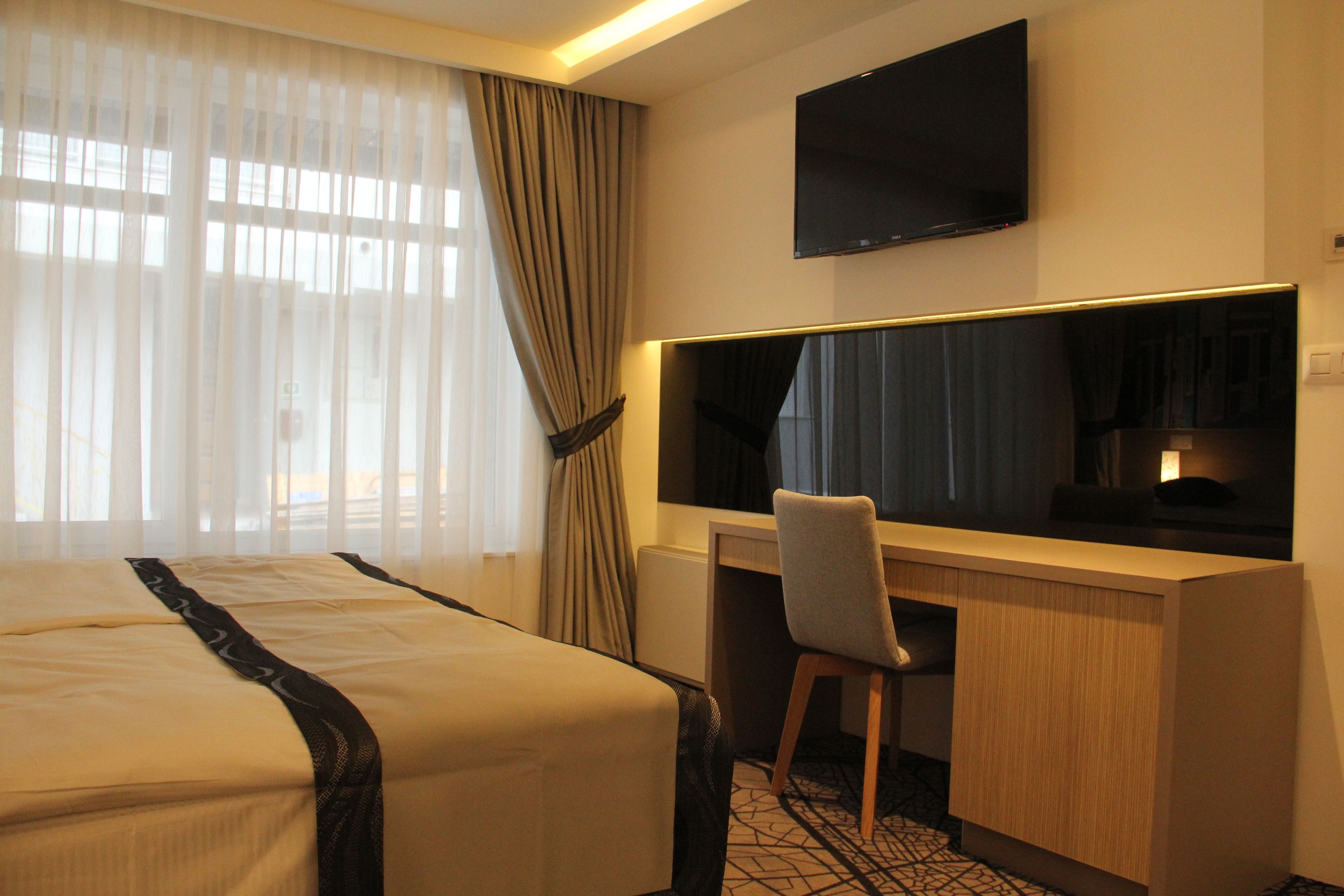 A hotel room with a bed, a desk, a chair, a TV, and a window with curtains.