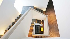 Un escalier moderne au design géométrique original, menant à un petit espace clos aménagé avec un canapé et une lampe.