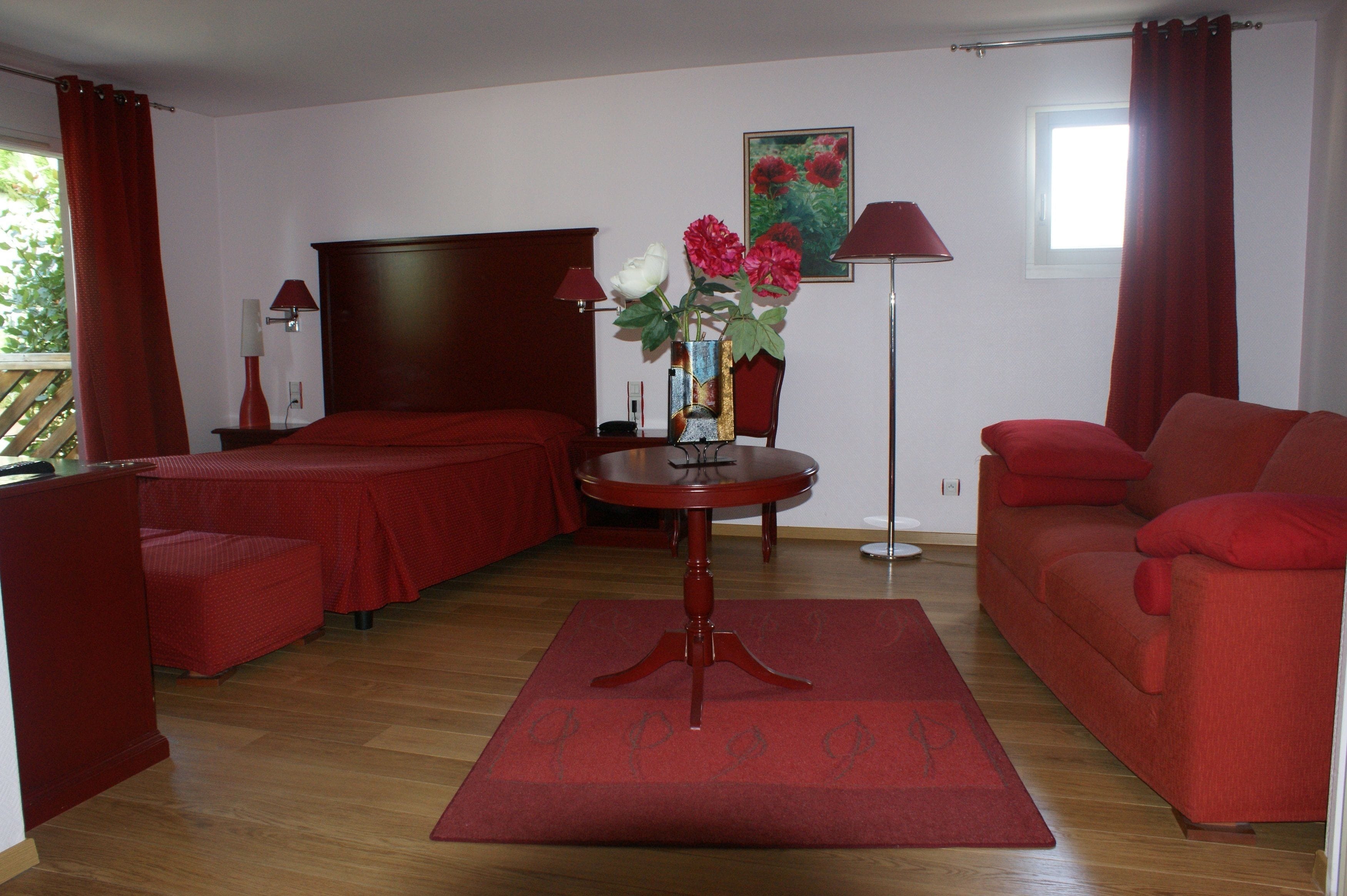 Une chambre d’hôtel avec un lit, un canapé, une table ornée d’un vase de fleurs et une lampe.