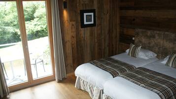 A bedroom with two beds, wooden walls, a large window, and a view of greenery outside.