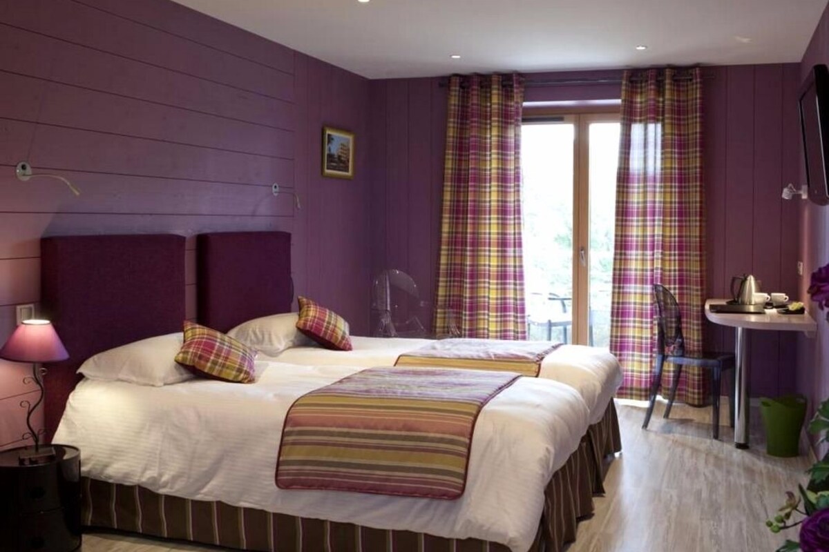 A hotel room with two beds, a desk, a chair, and a window with curtains.