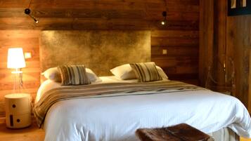 A wooden cabin bedroom with a large bed, a nightstand, a lamp, and a wooden bench.