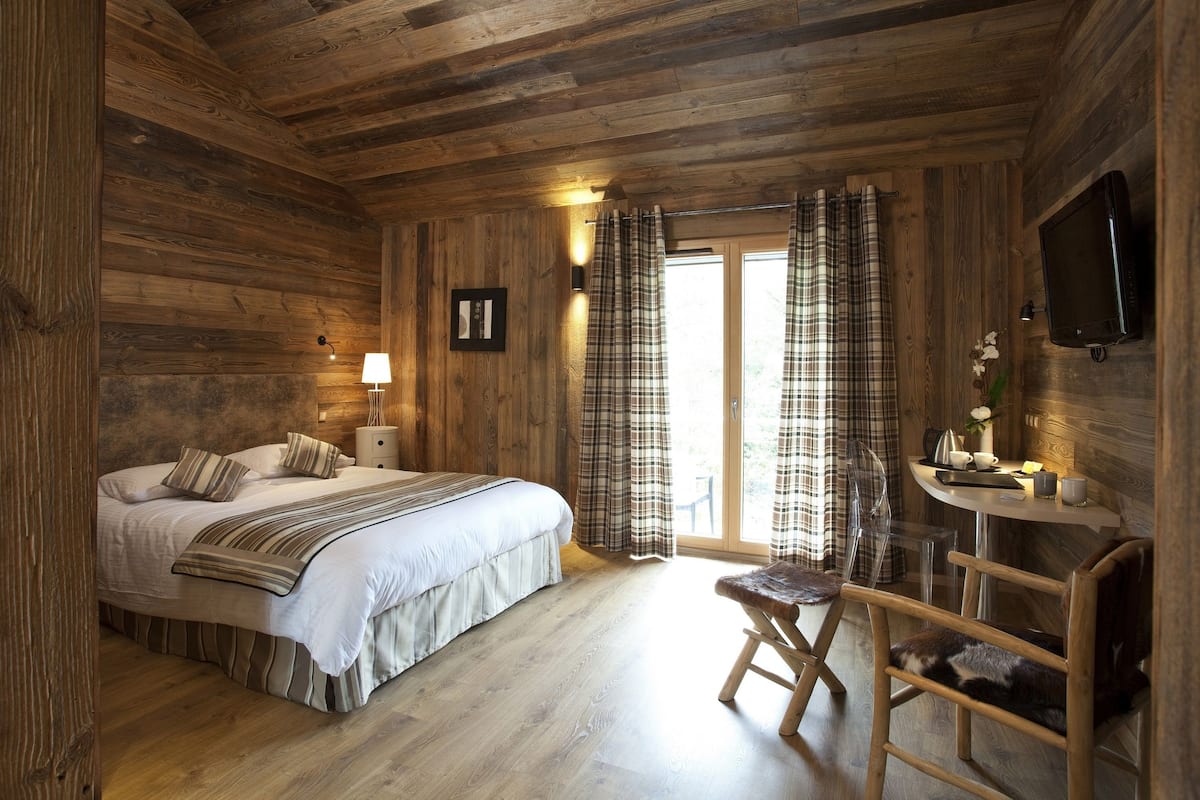 A wooden cabin bedroom with a bed, bedside table, lamp, and a TV mounted on the wall.