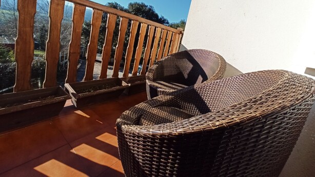 Una silla de mimbre en un balcón con baranda de madera, con vistas a un paisaje de árboles y cielo despejado.