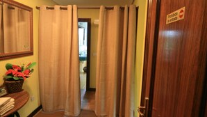Un pasillo de hotel con cortinas color beige, una puerta de madera con un letrero que dice 'Prohibida la entrada', un espejo y una mesita con una planta y toallas.