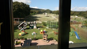 Vista de un parque infantil con diferentes juegos, una casita y una zona vallada.