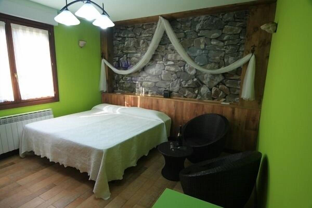 Una habitación con cama, una mesita, una silla y una pared de piedra.
