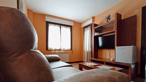 Una sala de estar con sofá, televisión, mesita y radiador.
