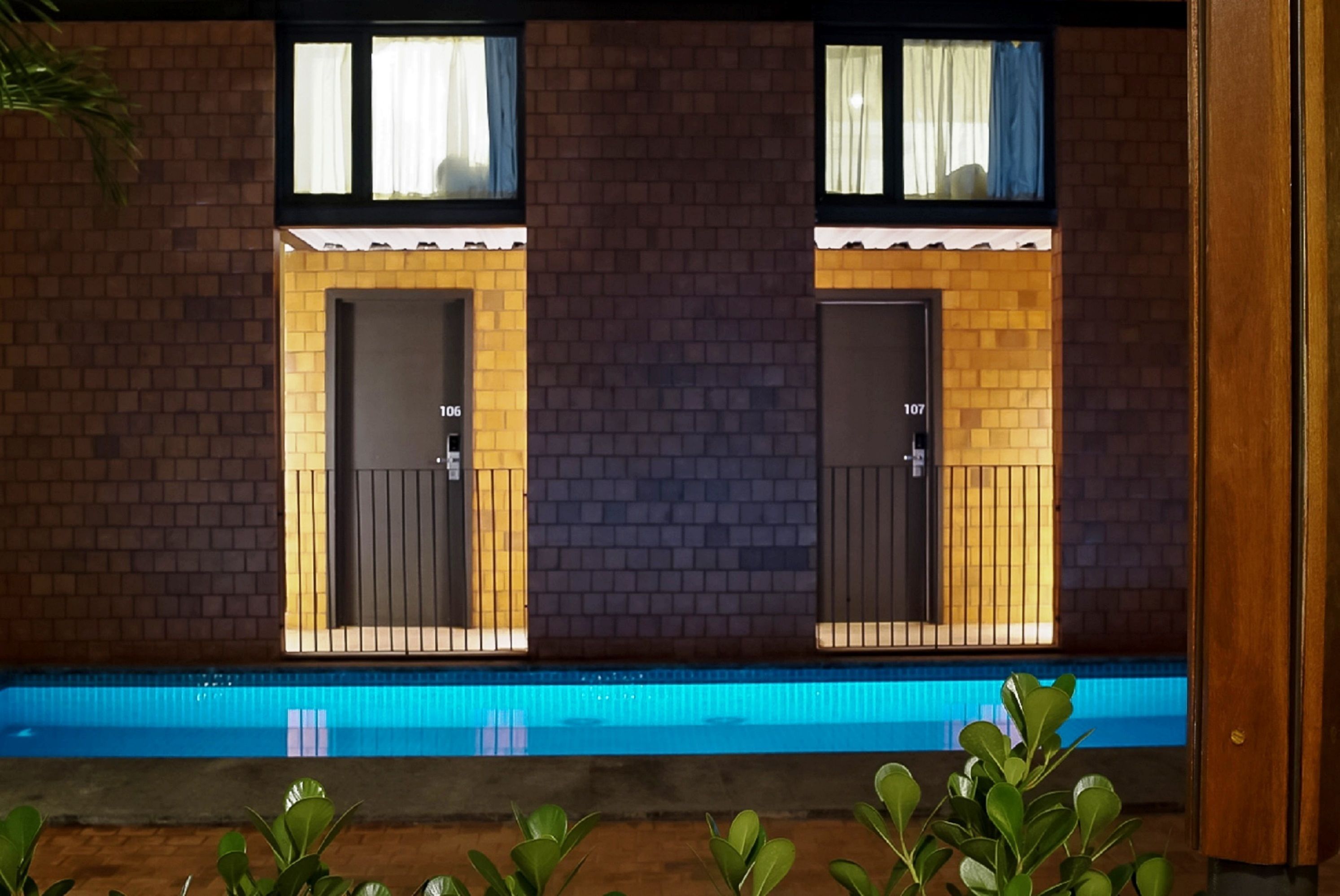 Un hotel con dos puertas, cada una con un número, y una piscina delantera.