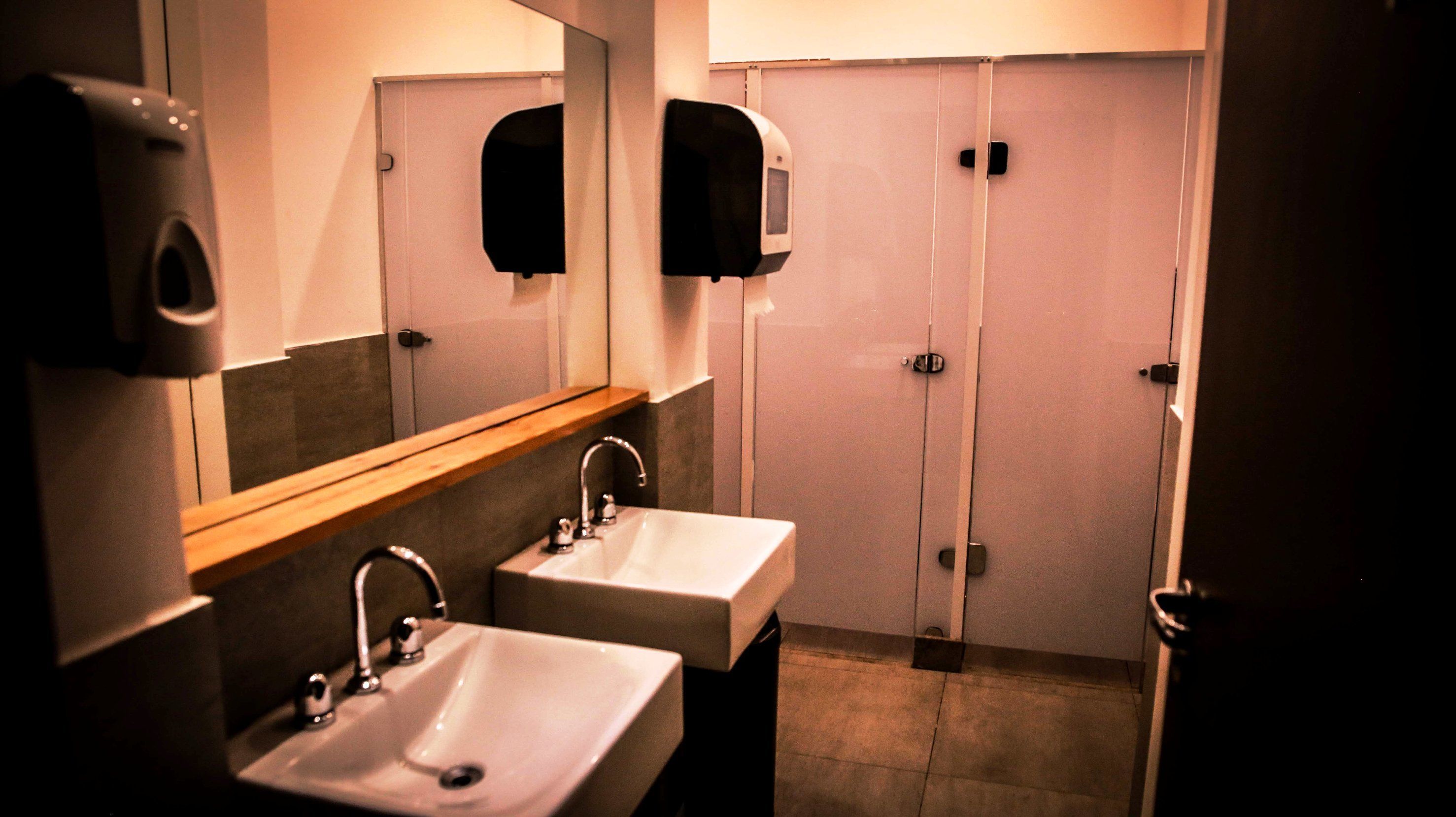 Baño público con dos lavamanos, un espejo y dispensadores de toallas de papel.