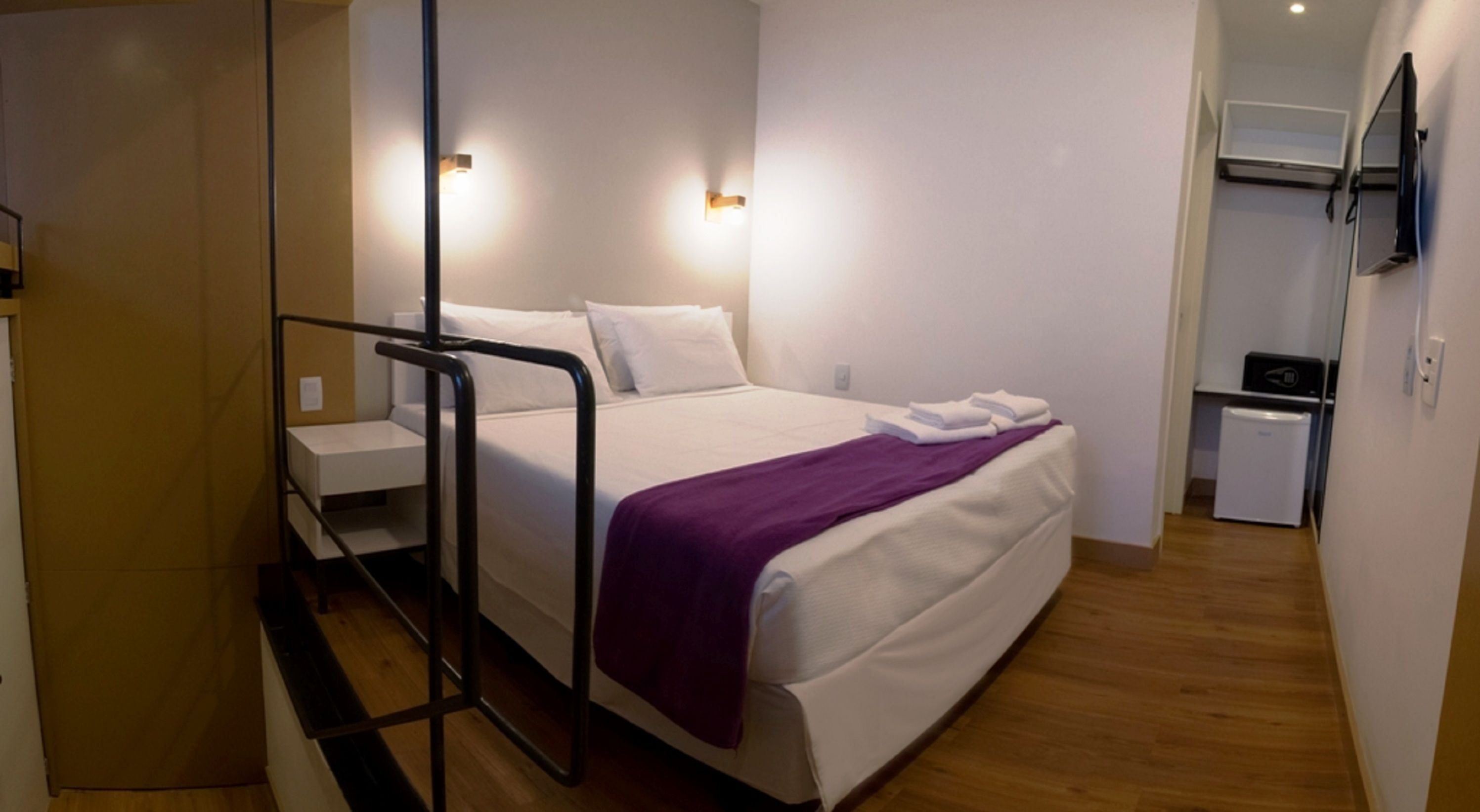 Et moderne hotelværelse med seng, et lille skrivebord, et spejl og et fjernsyn.