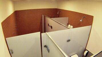 A restroom with two stalls, a shower area, and a toilet paper dispenser.