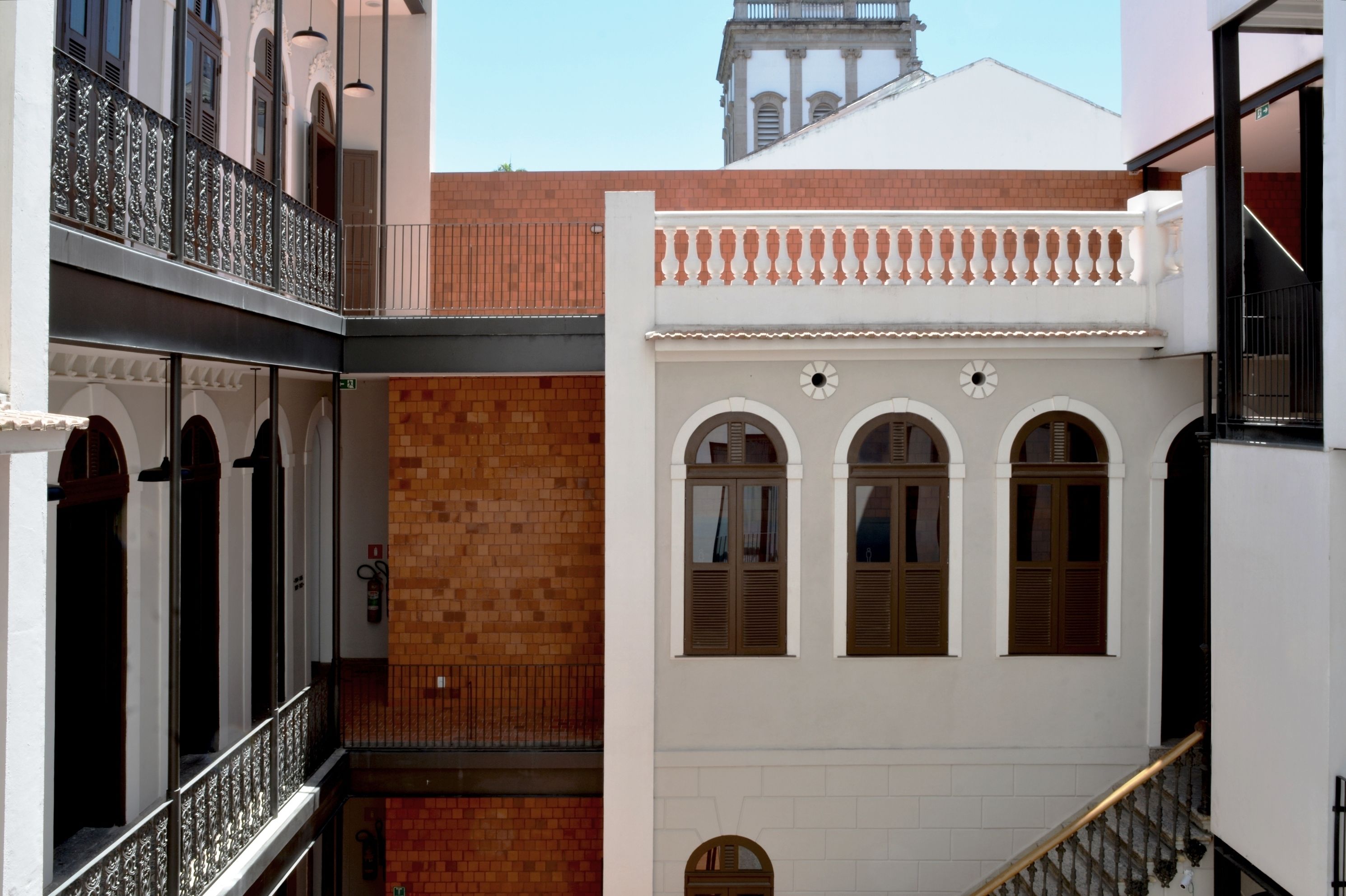 A multi-level building with a white facade, a brick wall, and a balcony with metal railings.