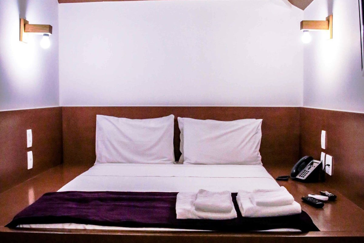Una habitación de hotel moderna con techo de madera, una cama grande con ropa de cama blanca, dos lámparas de noche y un teléfono en la mesita de noche.
