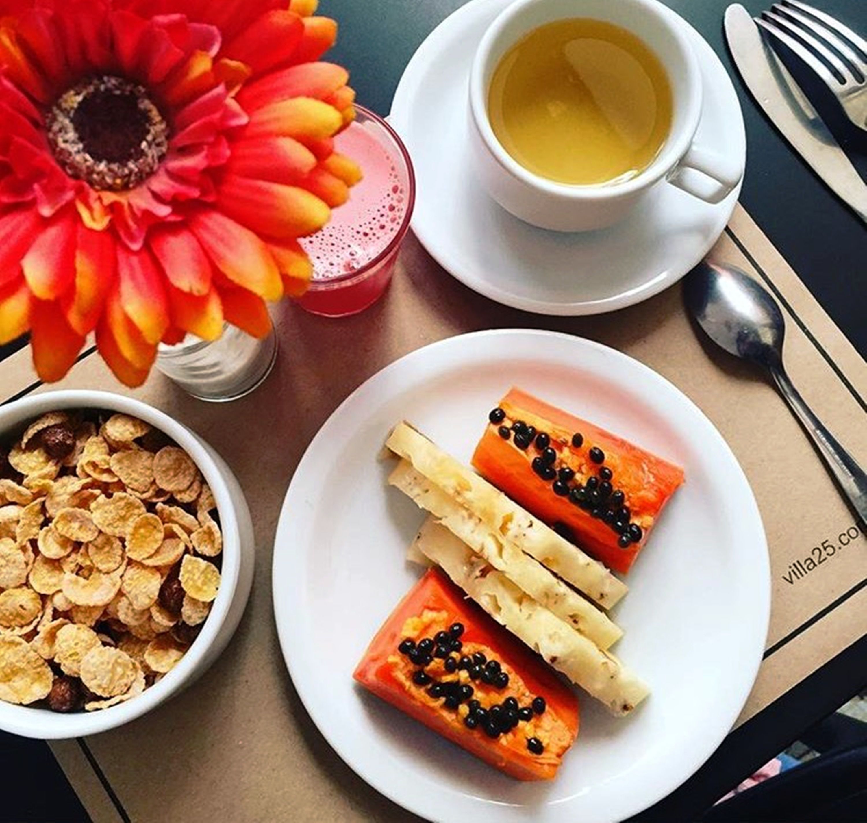 A table with a plate of food, a bowl of cereal, a cup of tea, and a glass of juice.