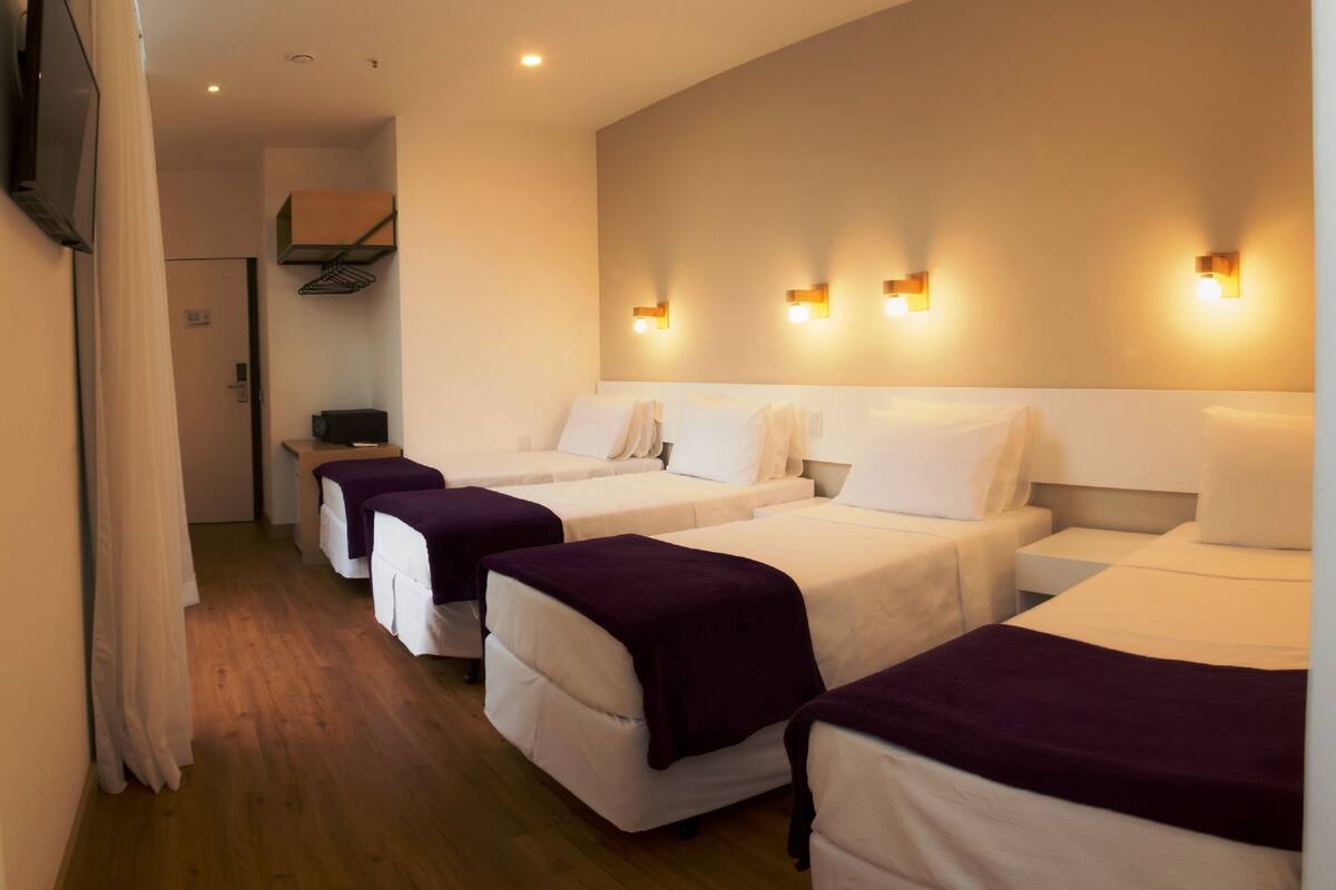 Habitación de hotel con cuatro camas individuales alineadas, piso de madera y un escritorio pequeño con una silla.