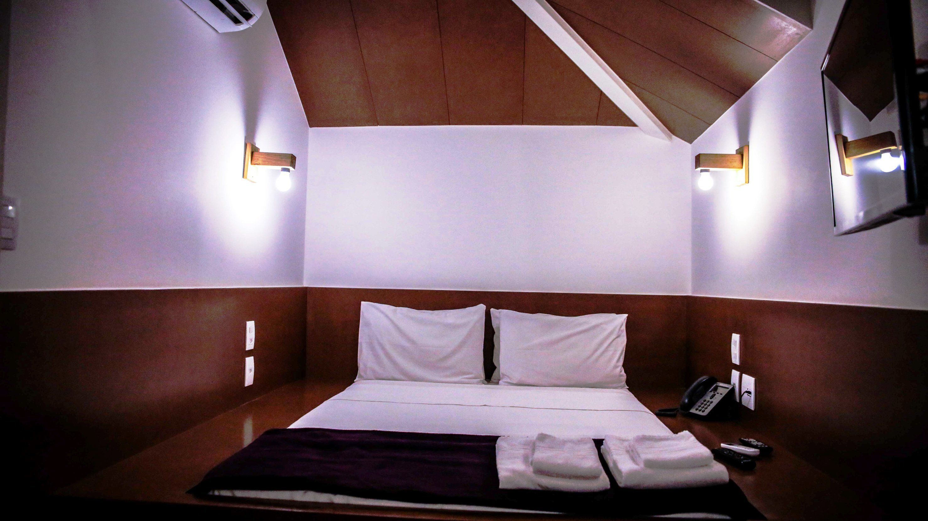 Een hotelkamer met een bed, twee bedlampen, een telefoon en een afstandsbediening op de nachtkastje.