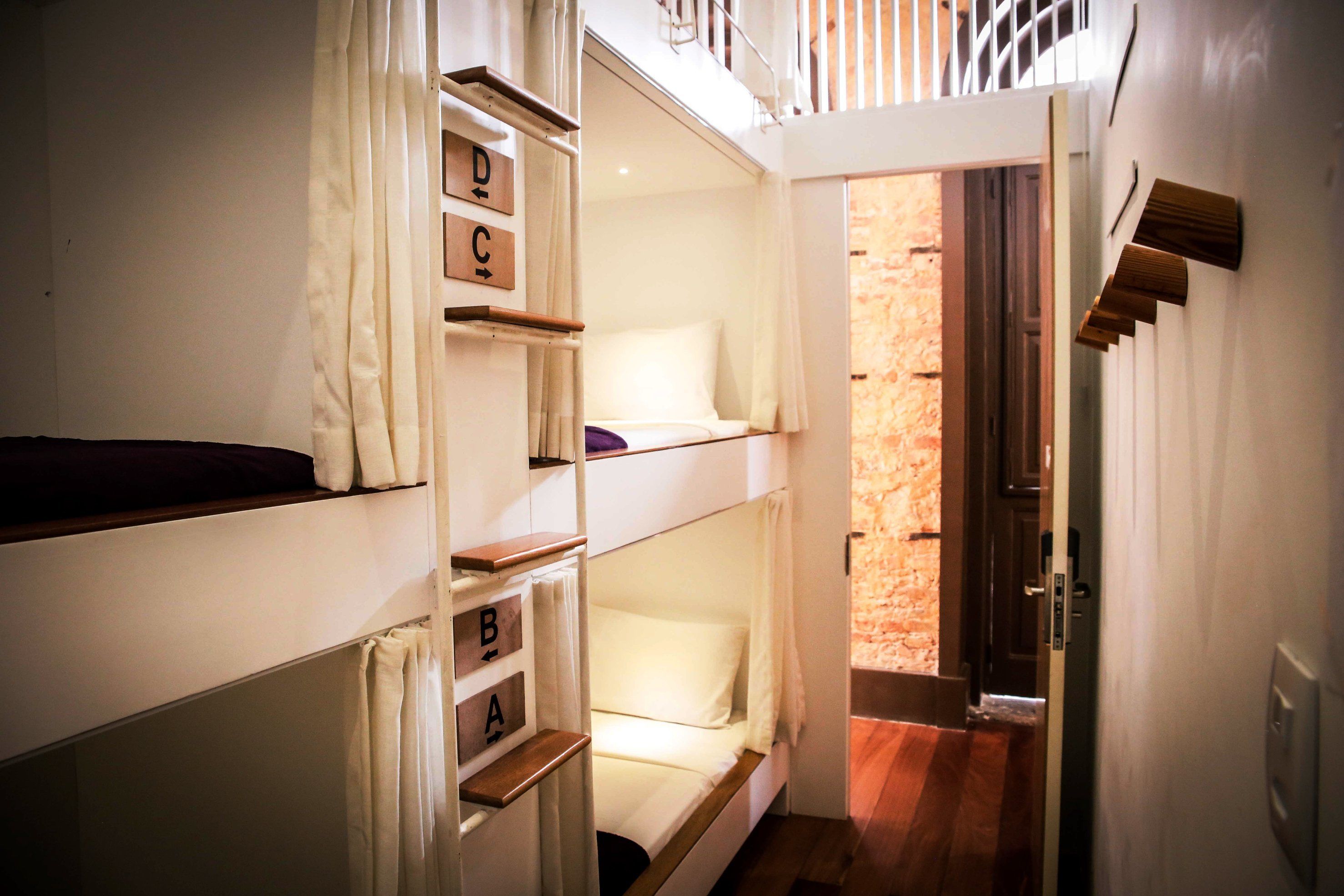 A bunk bed room with a wooden ladder and a door leading to a brick wall.