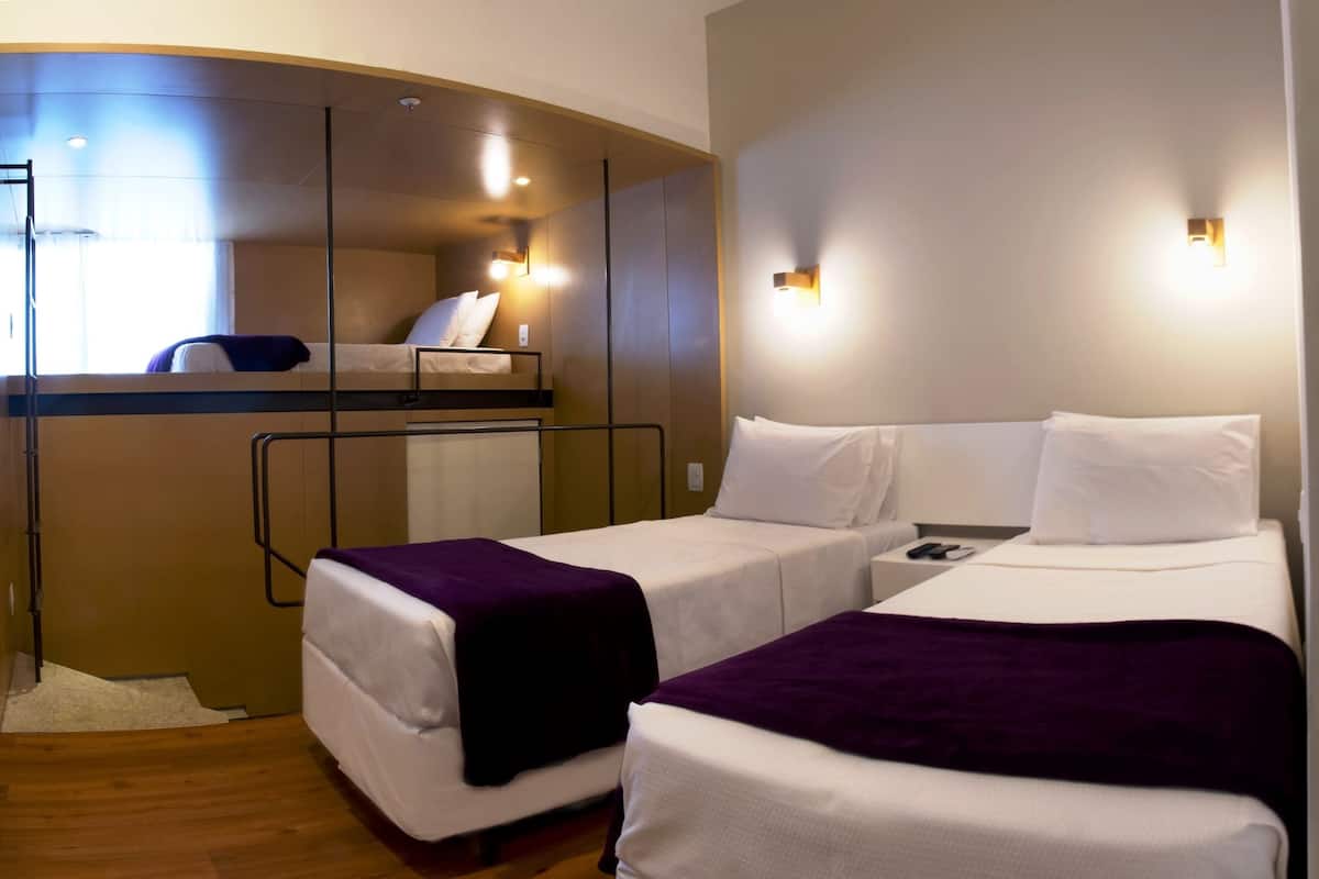 Una habitación de hotel con dos camas individuales, una litera, un escritorio pequeño y una ventana.
