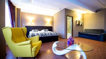 Una habitación de hotel con una cama, un sillón amarillo, un sofá azul y una mesa de centro de vidrio.