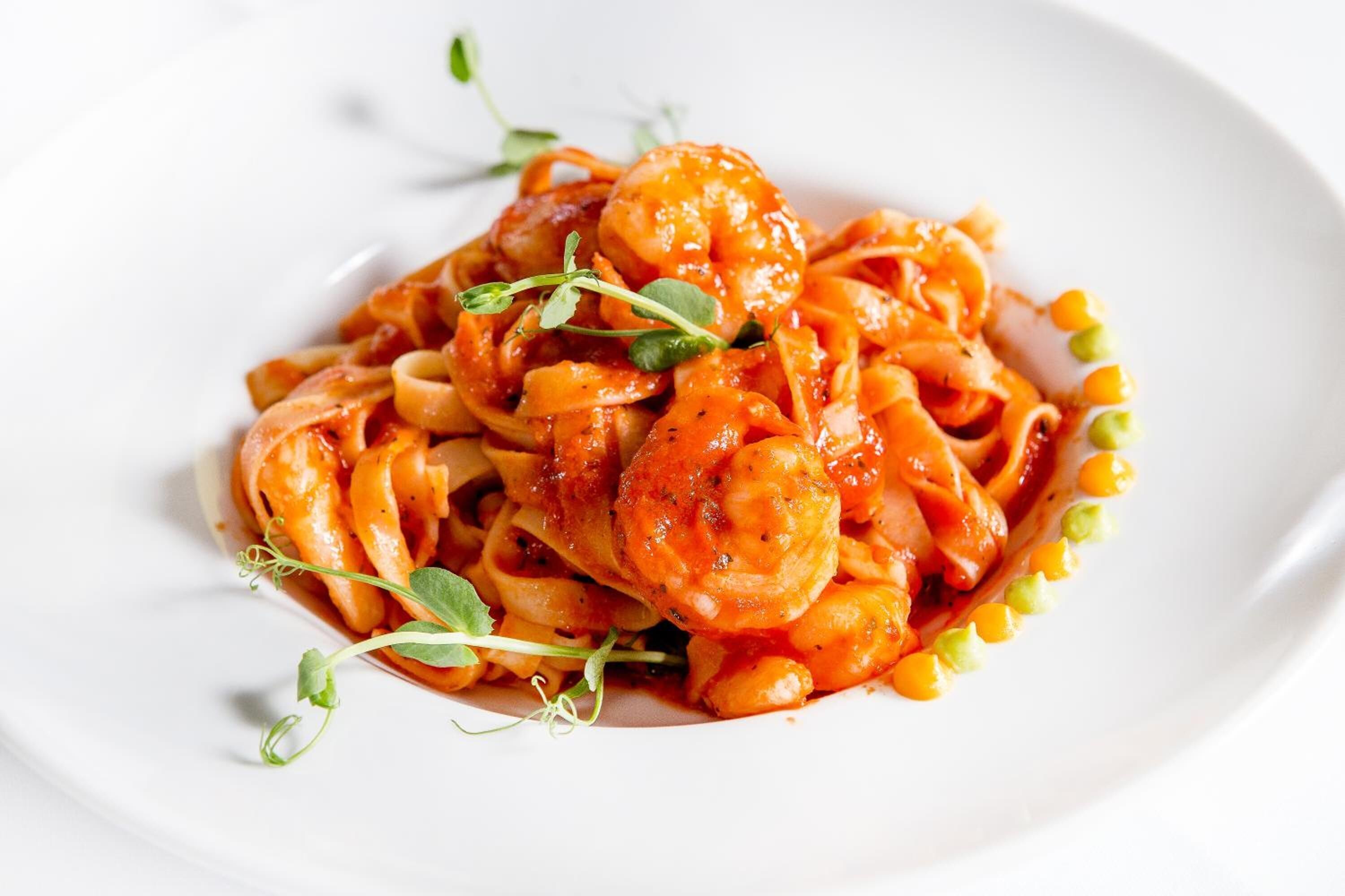A plate of pasta with shrimp and corn, garnished with microgreens.
