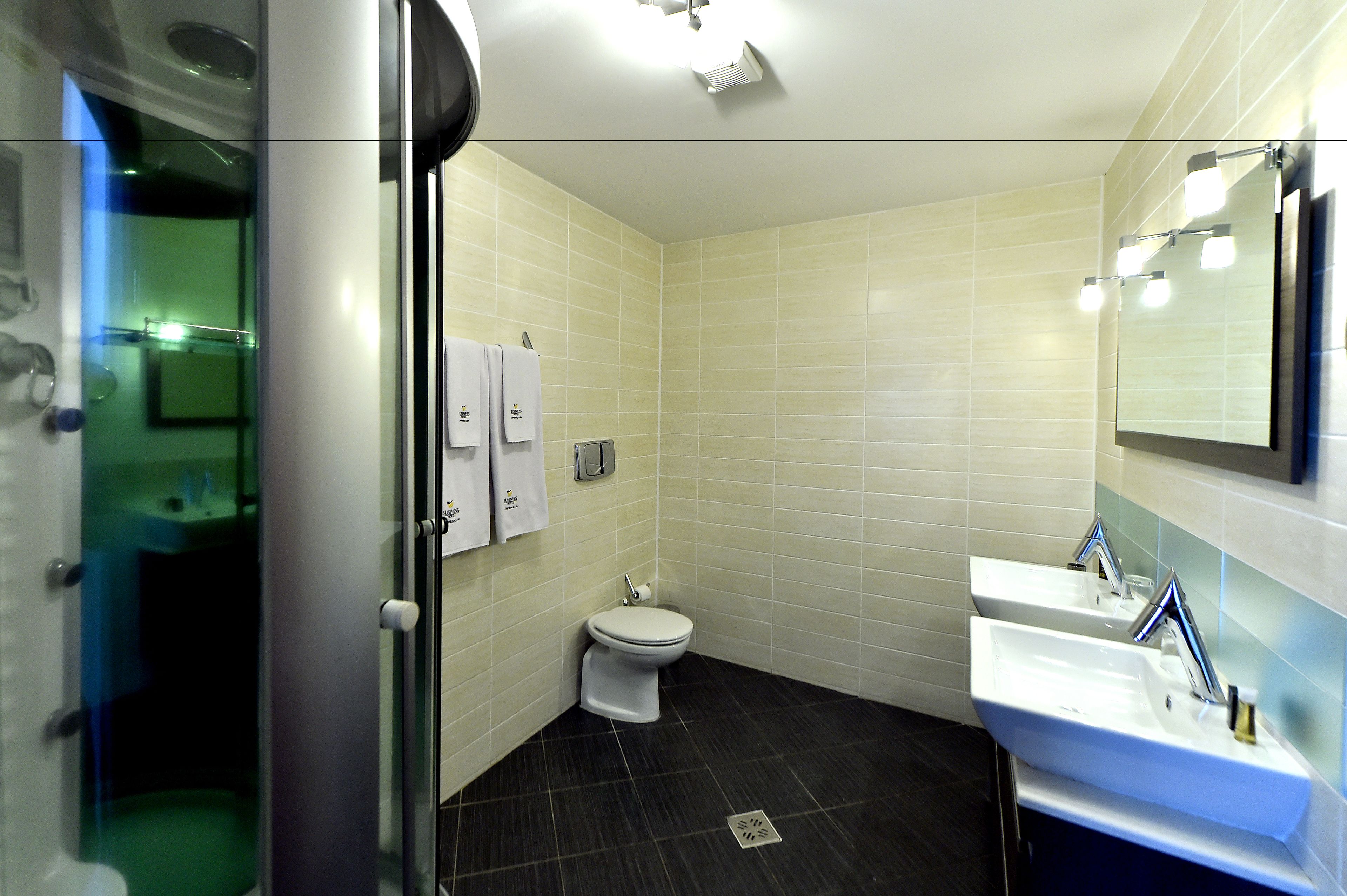A bathroom with a toilet, two sinks, a shower, and a glass-enclosed shower area.
