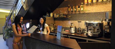 Zona de bar con barra, máquina de café espresso y estantes con botellas.