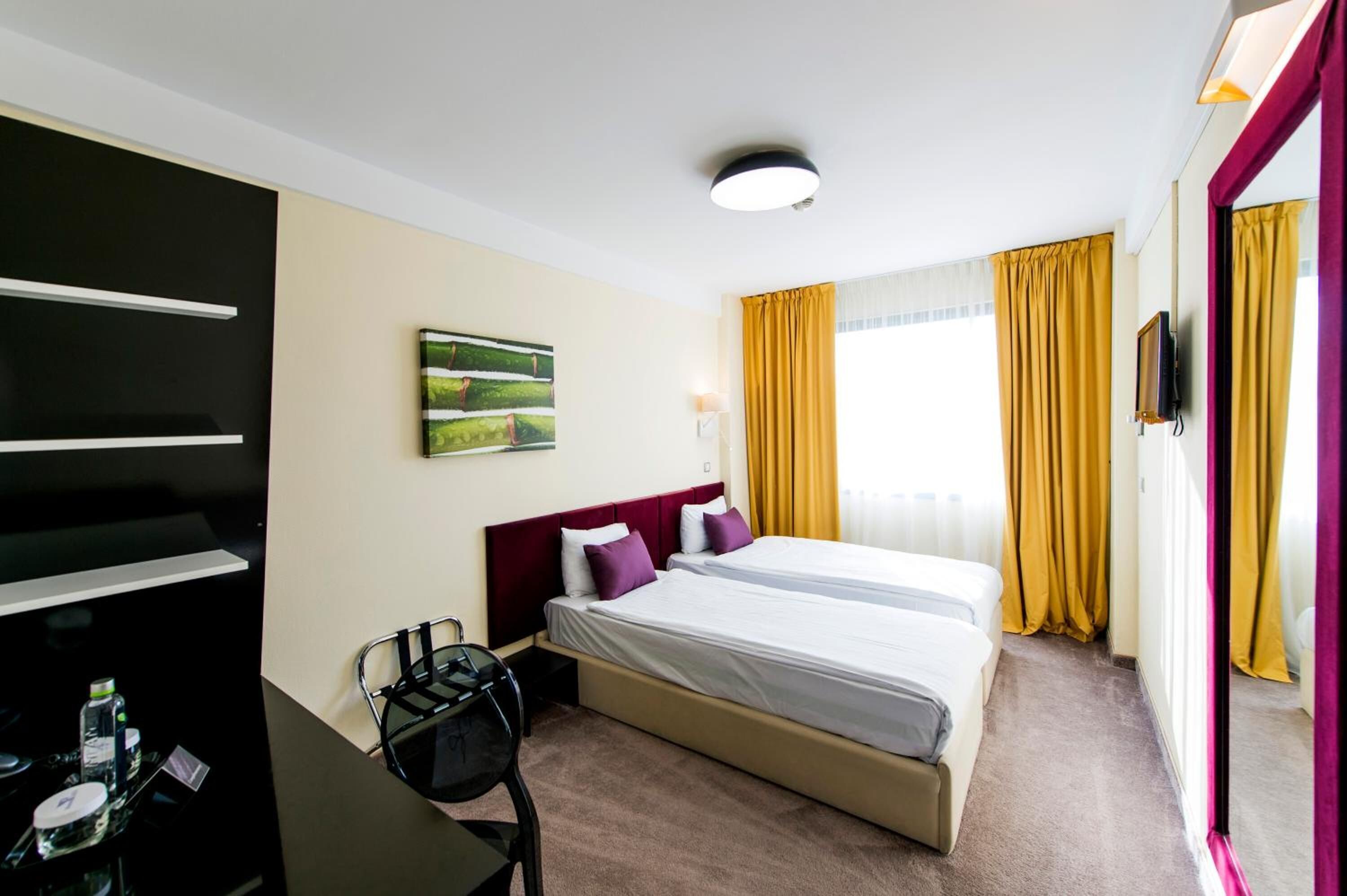 A hotel room with two beds, a desk with a chair, a flat-screen TV, and a painting on the wall.