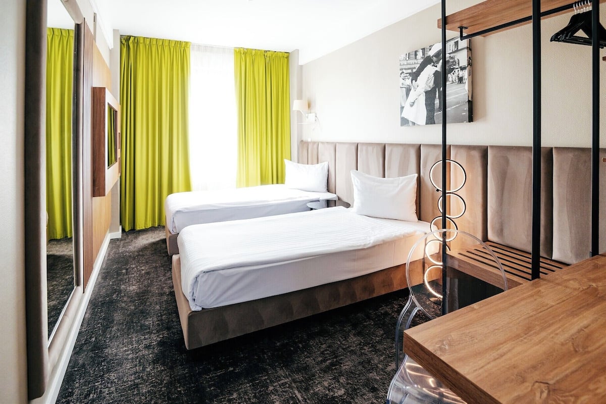 A hotel room with two beds, a wooden desk, a mirror, and a picture on the wall.
