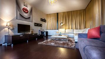 A modern living room with a flat-screen TV, dark wood flooring, a large sofa, a coffee table, and a decorative rug.