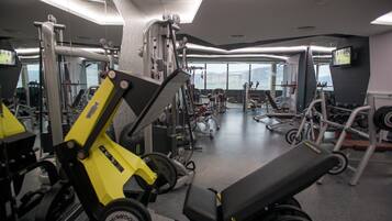 A gym with various exercise machines, a bench, and a large window providing a view of the outdoors.
