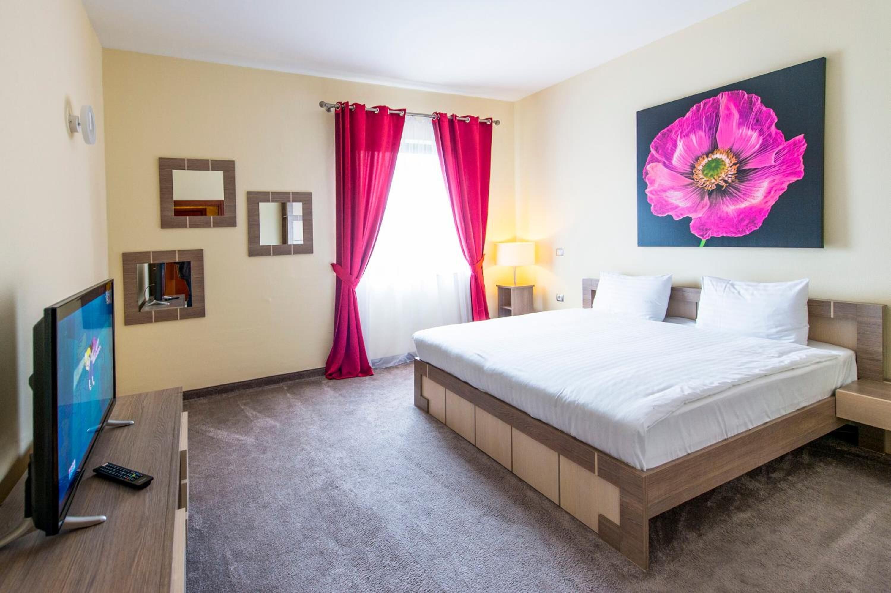 A hotel room with a large bed, a TV, a desk, and a painting of a flower on the wall.