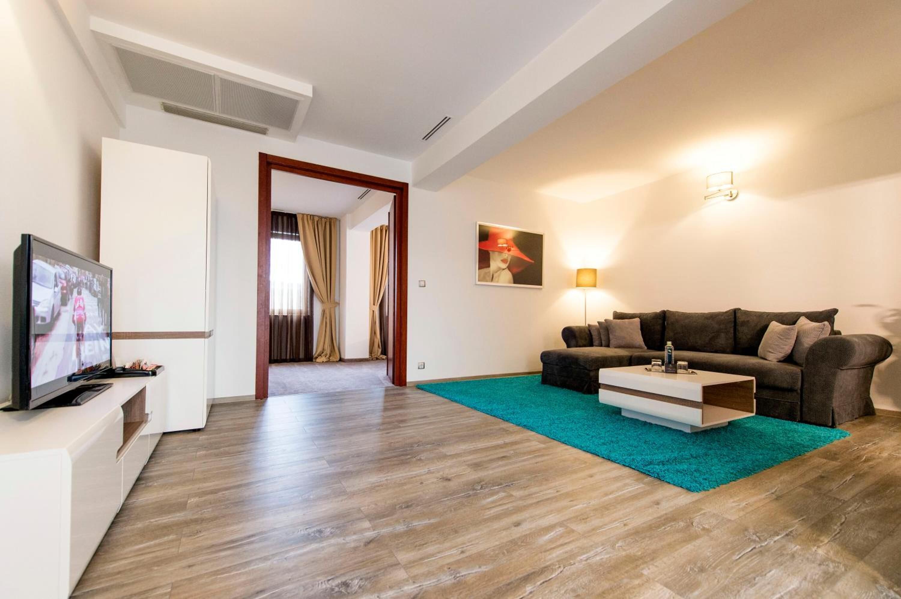 Un salon moderne avec un téléviseur à écran plat, un canapé marron, un tapis turquoise et une table basse en bois.